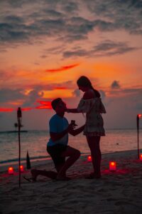 man kneeling in front of a woman by the beach during golden hour